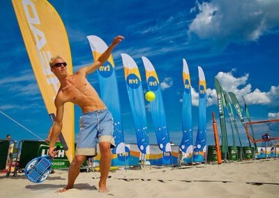 Custom flags featuring sponsor logos, including TVN, at a beach pickleball tournament, enhancing the event's branding and visibility.